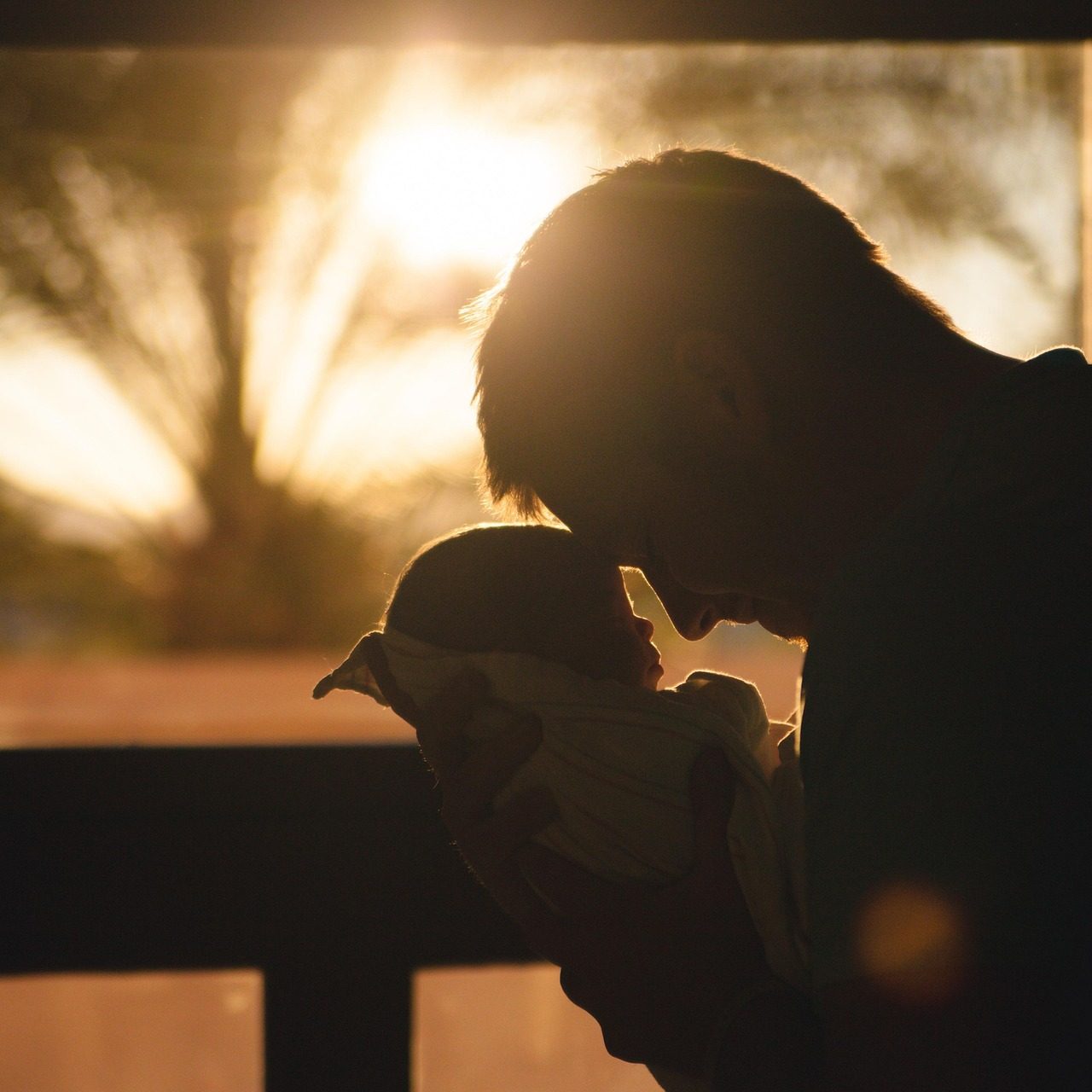 Vater hält neugeborenes Baby in der Dämmerung, sanftes Licht im Hintergrund.