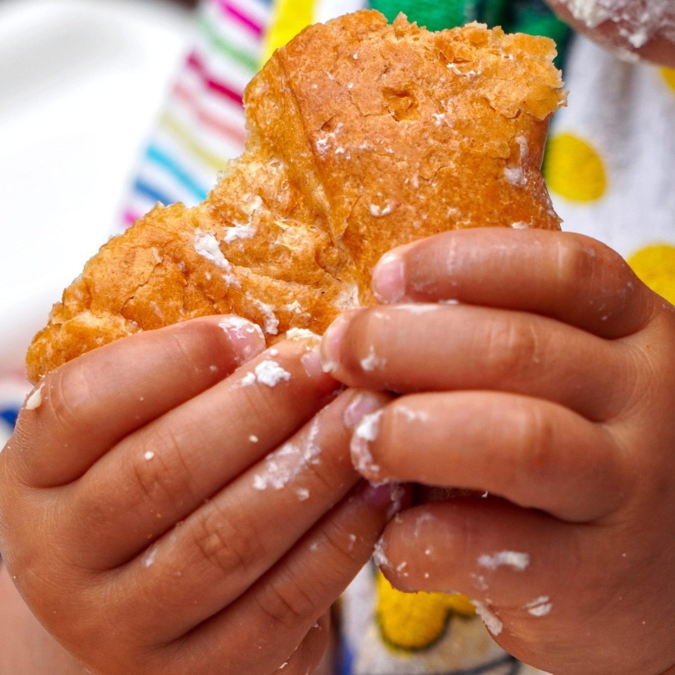 Kinderhände halten ein Stück süßes Gebäck, mit Puderzucker bestäubt.