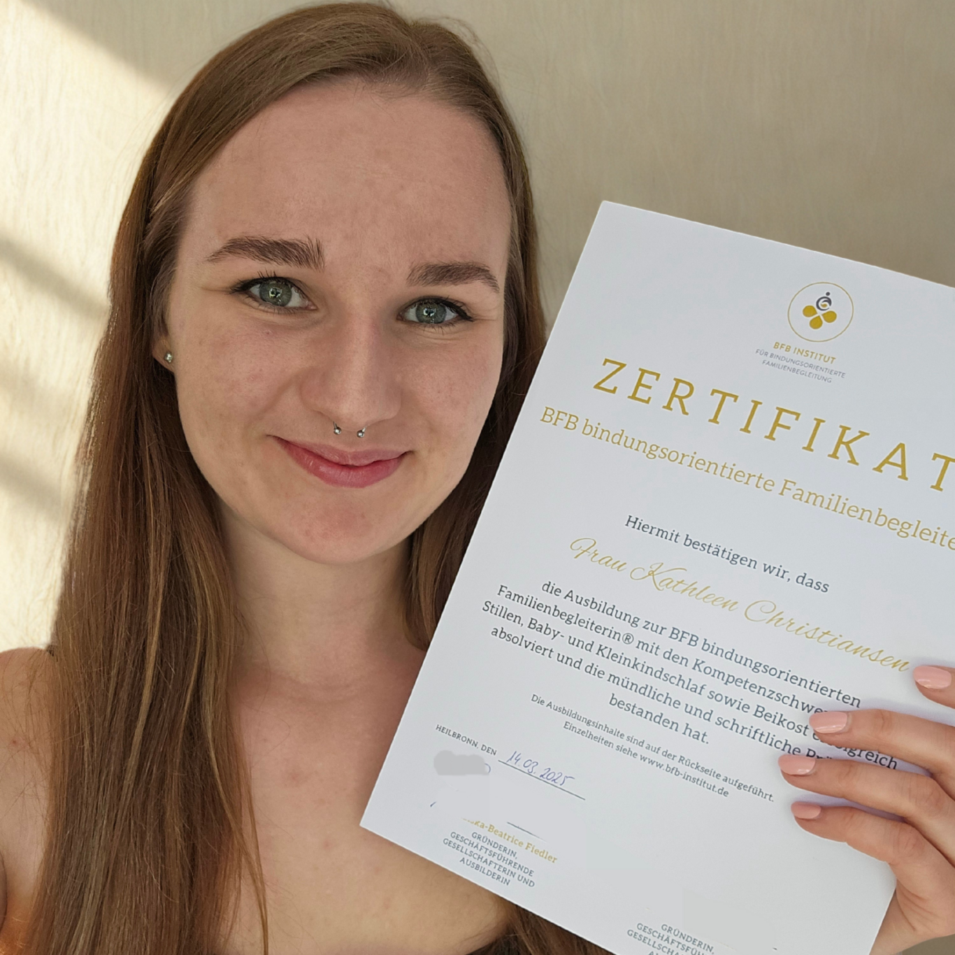 Junge Frau hält ein Zertifikat in der Hand und lächelt.